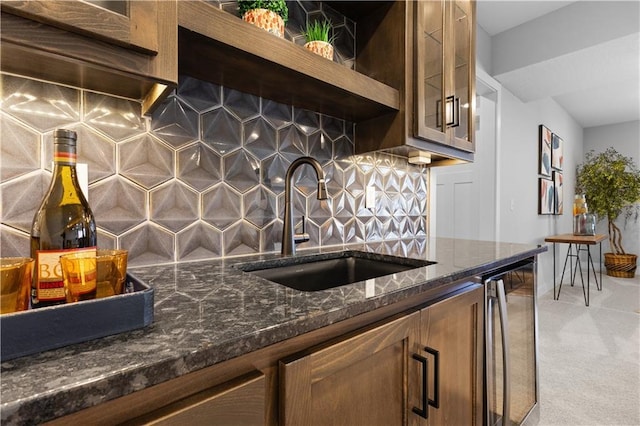 kitchen featuring dark stone counters, glass insert cabinets, light colored carpet, a sink, and backsplash