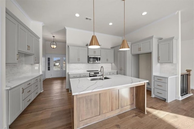 kitchen with light stone counters, visible vents, a sink, stainless steel microwave, and decorative backsplash
