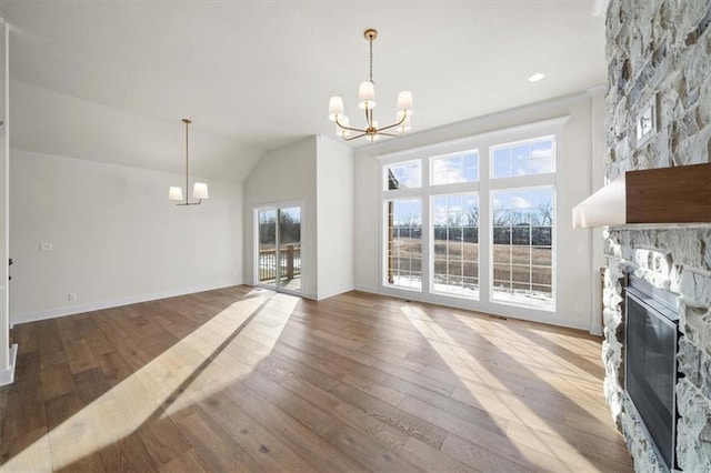 unfurnished dining area featuring vaulted ceiling, a stone fireplace, a chandelier, baseboards, and hardwood / wood-style flooring