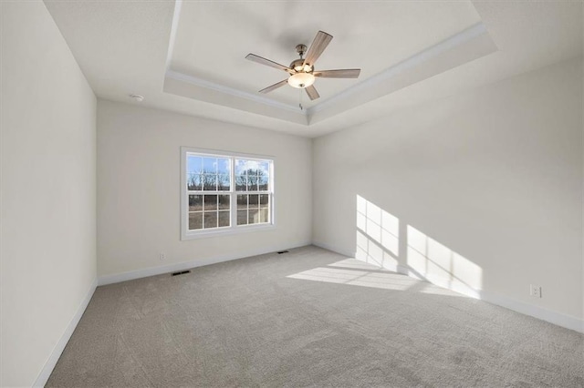 empty room featuring visible vents, baseboards, a raised ceiling, a ceiling fan, and carpet flooring