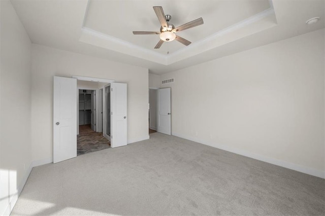 unfurnished bedroom with light carpet, a tray ceiling, visible vents, ceiling fan, and a walk in closet