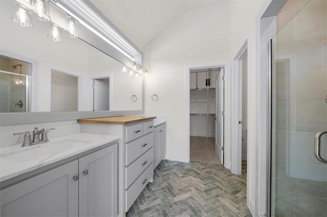 bathroom featuring vaulted ceiling, a shower stall, brick floor, vanity, and a walk in closet