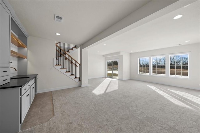 unfurnished living room featuring visible vents, a sink, recessed lighting, stairs, and light colored carpet