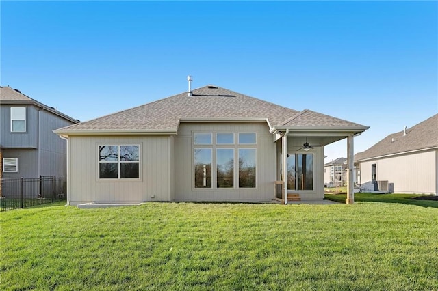 back of property with roof with shingles, central AC unit, fence, a ceiling fan, and a yard