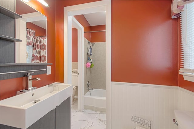 full bathroom featuring toilet, marble finish floor, shower / tub combo with curtain, wainscoting, and vanity