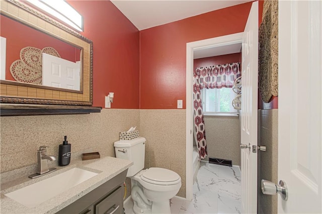 bathroom featuring tile walls, toilet, marble finish floor, wainscoting, and vanity