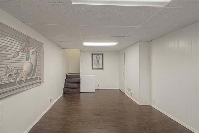 finished below grade area with a drop ceiling, baseboards, stairway, and wood finished floors