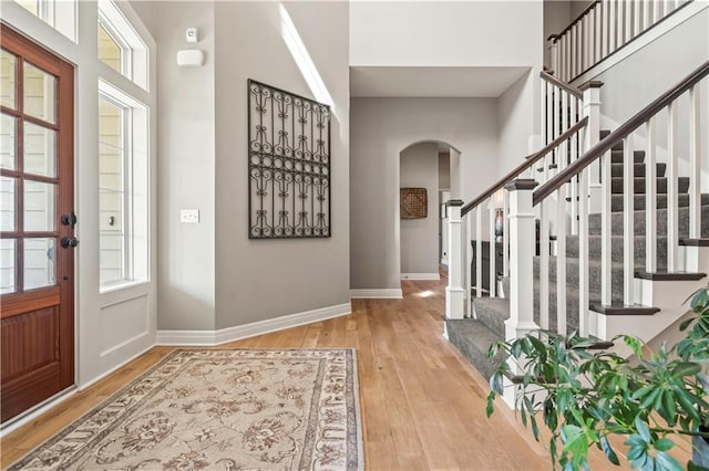 entryway with arched walkways, a towering ceiling, stairs, wood-type flooring, and baseboards