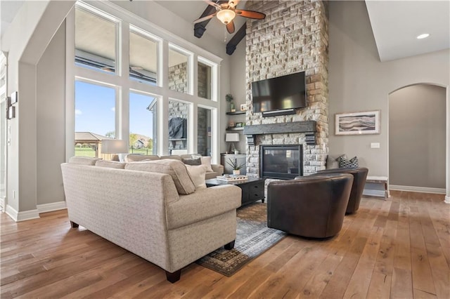 living area featuring arched walkways, a ceiling fan, a stone fireplace, and hardwood / wood-style flooring