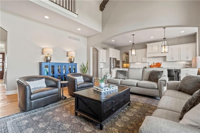 living room featuring arched walkways, a towering ceiling, visible vents, wood finished floors, and baseboards