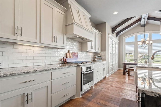kitchen featuring tasteful backsplash, an inviting chandelier, lofted ceiling with beams, wood finished floors, and stainless steel appliances