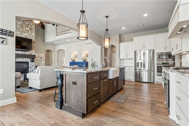kitchen with open floor plan, dark brown cabinets, stainless steel appliances, arched walkways, and a sink