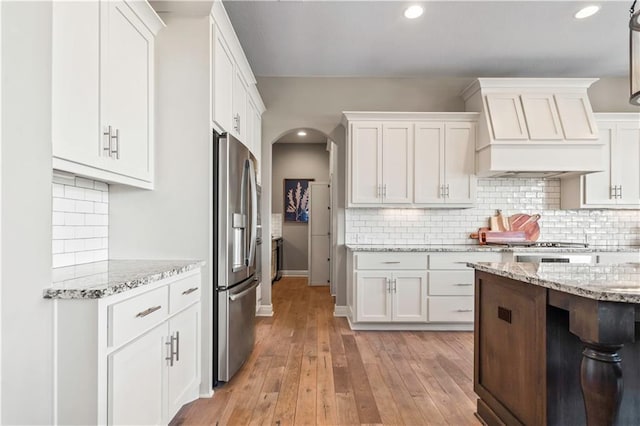 kitchen featuring white cabinetry, custom range hood, appliances with stainless steel finishes, and light wood finished floors