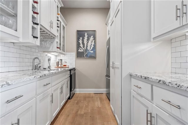 kitchen with light wood-style floors, dishwashing machine, tasteful backsplash, white cabinetry, and a sink