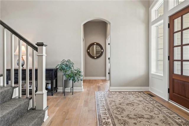 foyer entrance featuring arched walkways, stairs, light wood finished floors, and baseboards