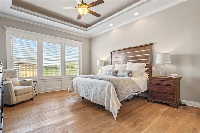 bedroom featuring crown molding, a tray ceiling, and light wood-type flooring