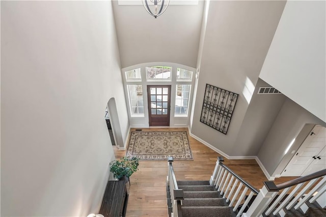 entryway with a towering ceiling, baseboards, visible vents, arched walkways, and wood finished floors