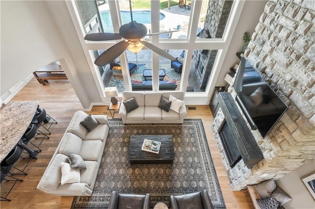 living room with ceiling fan, a high ceiling, baseboards, and wood finished floors
