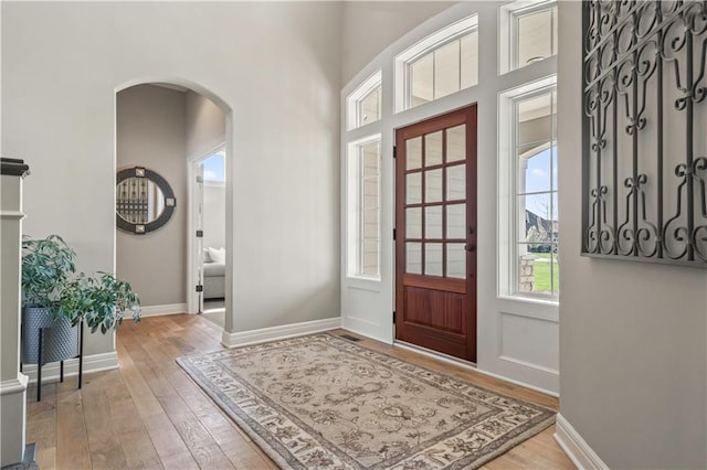 foyer entrance featuring arched walkways, light wood-style flooring, and baseboards