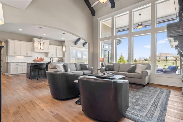 living room with ceiling fan, light wood-type flooring, arched walkways, and a towering ceiling