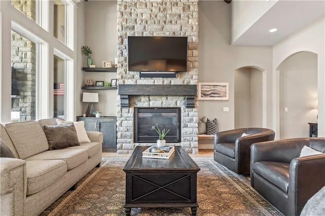 living room featuring a stone fireplace, arched walkways, a high ceiling, and wood finished floors