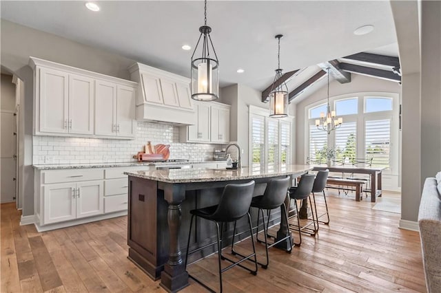 kitchen featuring light wood finished floors, premium range hood, white cabinetry, and decorative backsplash