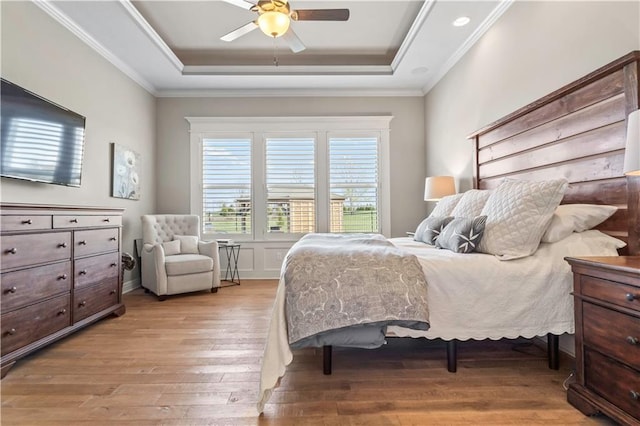bedroom with ornamental molding, a tray ceiling, and light wood finished floors
