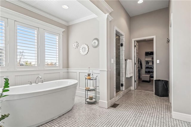 bathroom with a stall shower, a soaking tub, crown molding, a wainscoted wall, and a walk in closet