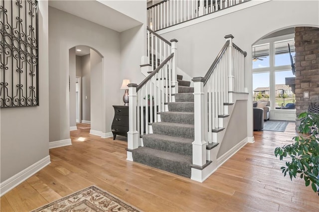 stairs featuring arched walkways, a towering ceiling, a ceiling fan, baseboards, and hardwood / wood-style flooring