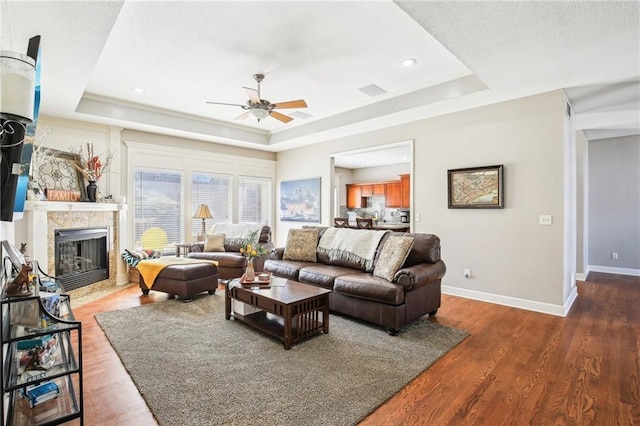 living area featuring ceiling fan, a raised ceiling, a premium fireplace, baseboards, and wood finished floors