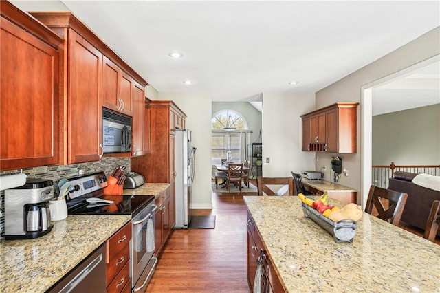 kitchen featuring light stone counters, decorative backsplash, stainless steel appliances, and dark wood-type flooring