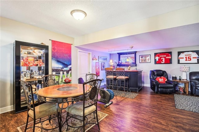 dining space with a bar, a textured ceiling, baseboards, and wood finished floors
