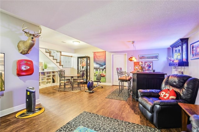 living area featuring a textured ceiling, stairs, baseboards, wood finished floors, and a bar