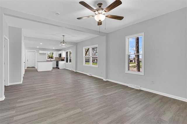 unfurnished living room with visible vents, baseboards, ceiling fan, and dark wood-style floors