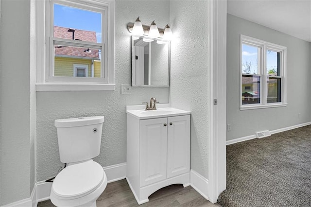bathroom with vanity, visible vents, toilet, wood finished floors, and a textured wall