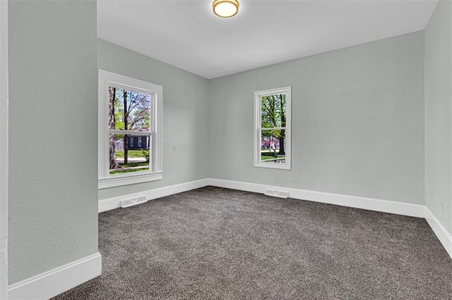 unfurnished room with dark carpet, visible vents, and plenty of natural light