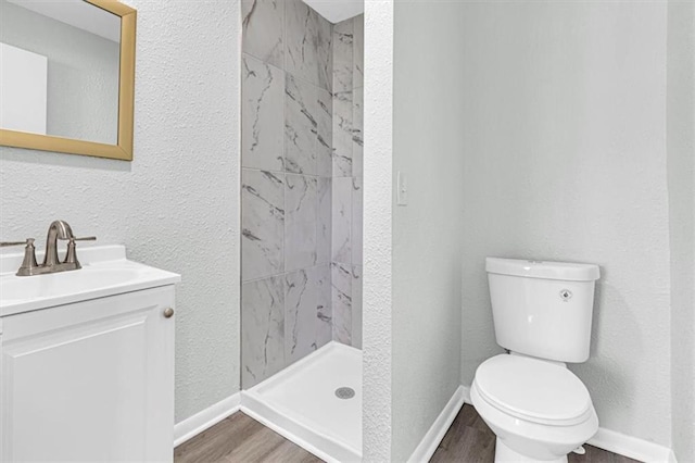 full bath with vanity, a stall shower, a textured wall, toilet, and wood finished floors