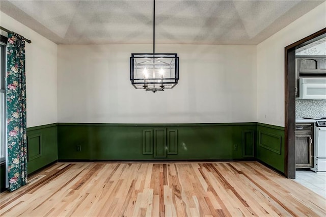 12253 W 104th St, Lenexa, KS 66215 - unfurnished dining area with light wood-style floors, wainscoting, a textured ceiling, and a chandelier