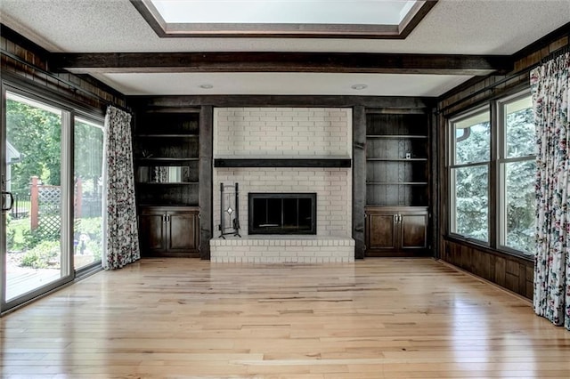 12253 W 104th St, Lenexa, KS 66215 - unfurnished living room featuring beamed ceiling, light wood-style floors, built in features, a textured ceiling, and a brick fireplace