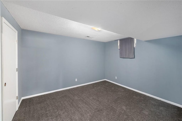 finished below grade area with dark carpet, baseboards, and a textured ceiling