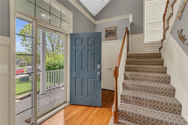 foyer featuring light wood-style floors, a decorative wall, wainscoting, and vaulted ceiling