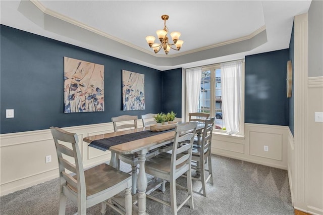 carpeted dining room featuring crown molding, a raised ceiling, a wainscoted wall, and a notable chandelier