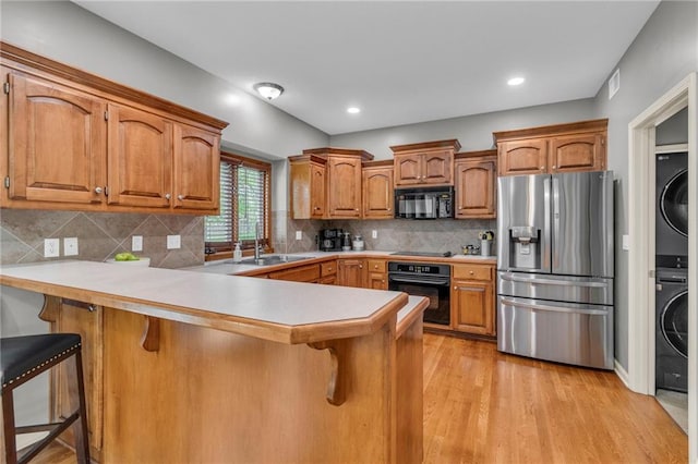 kitchen featuring stacked washer / drying machine, a sink, a breakfast bar area, a peninsula, and black appliances