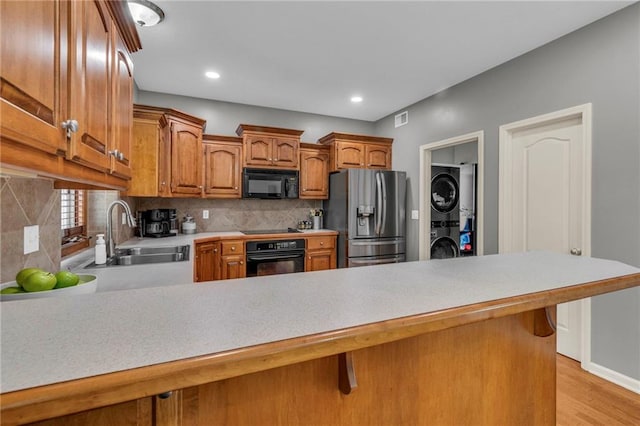 kitchen with a peninsula, stacked washing maching and dryer, light countertops, a sink, and black appliances