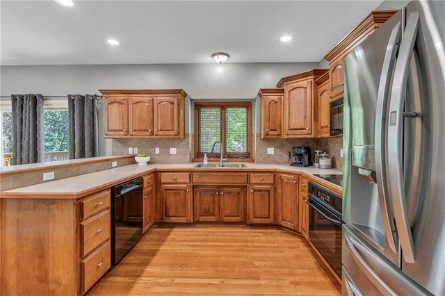 kitchen featuring a sink, black appliances, light wood-style flooring, and a wealth of natural light