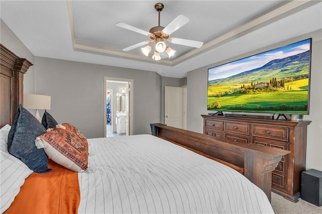 carpeted bedroom featuring a raised ceiling, ceiling fan, and ensuite bath