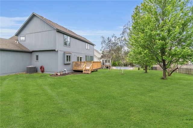 rear view of property with central AC unit, a wooden deck, a yard, and fence