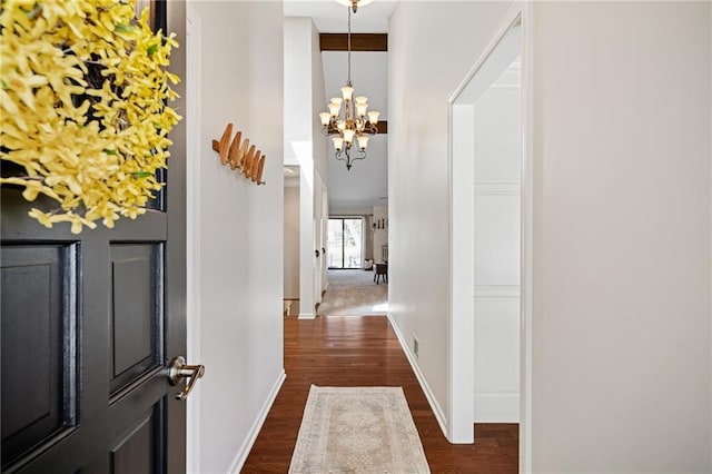 hall featuring a chandelier, dark wood-type flooring, a towering ceiling, and baseboards
