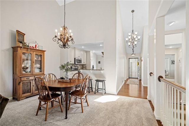 dining area with light carpet, a high ceiling, a notable chandelier, and baseboards