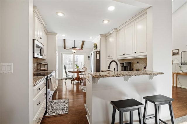 kitchen featuring ceiling fan, appliances with stainless steel finishes, a peninsula, backsplash, and a breakfast bar area
